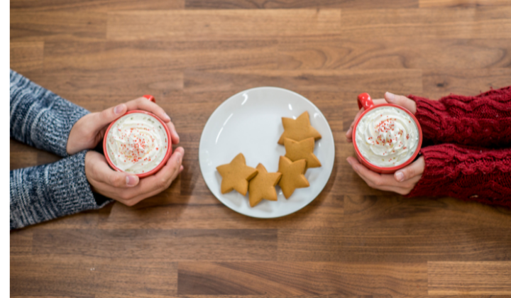 Couple's hands holding hot cocoa with cookies on a plate in between