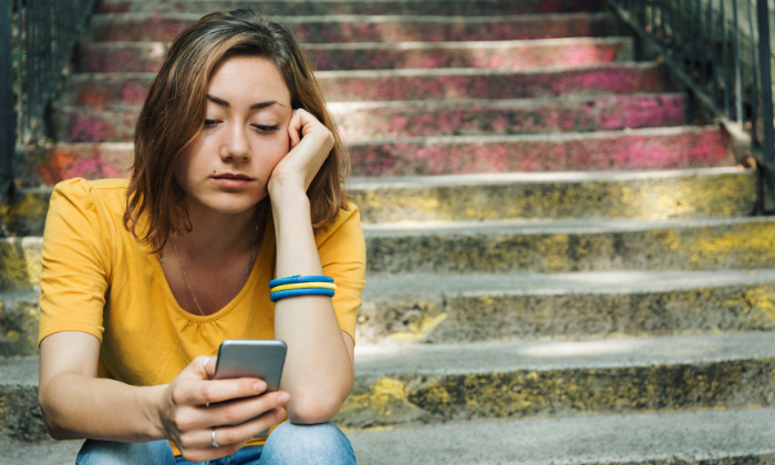 Young woman scrolling her cell phone with a look of sadness
